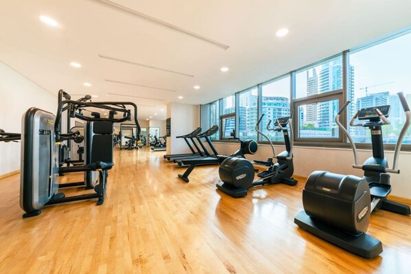 Un gimnasio con diferentes equipos de ejercicio, ventanas amplias y piso de madera.
