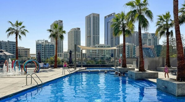 A swimming pool with a cityscape in the background, surrounded by palm trees and modern buildings.