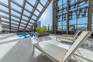 Un área de piscina en la azotea con sillones de descanso y un pequeño jardín.