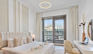 A modern hotel room with a large bed, a desk with a laptop, and a view of the city through large windows.