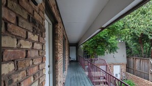 Un portico coperto con un muro in mattoni, un pavimento in legno e una ringhiera in metallo.