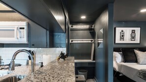 Una cucina compatta con piano di lavoro in granito, lavello in acciaio inossidabile e forno a microonde. Sul piano si trova una piccola moto, e al muro c'è una cornice con fotografie di macchine fotografiche.