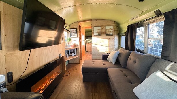 Interior acogedor de una autocaravana con televisión de pantalla plana, un sofá y una pequeña cocina.