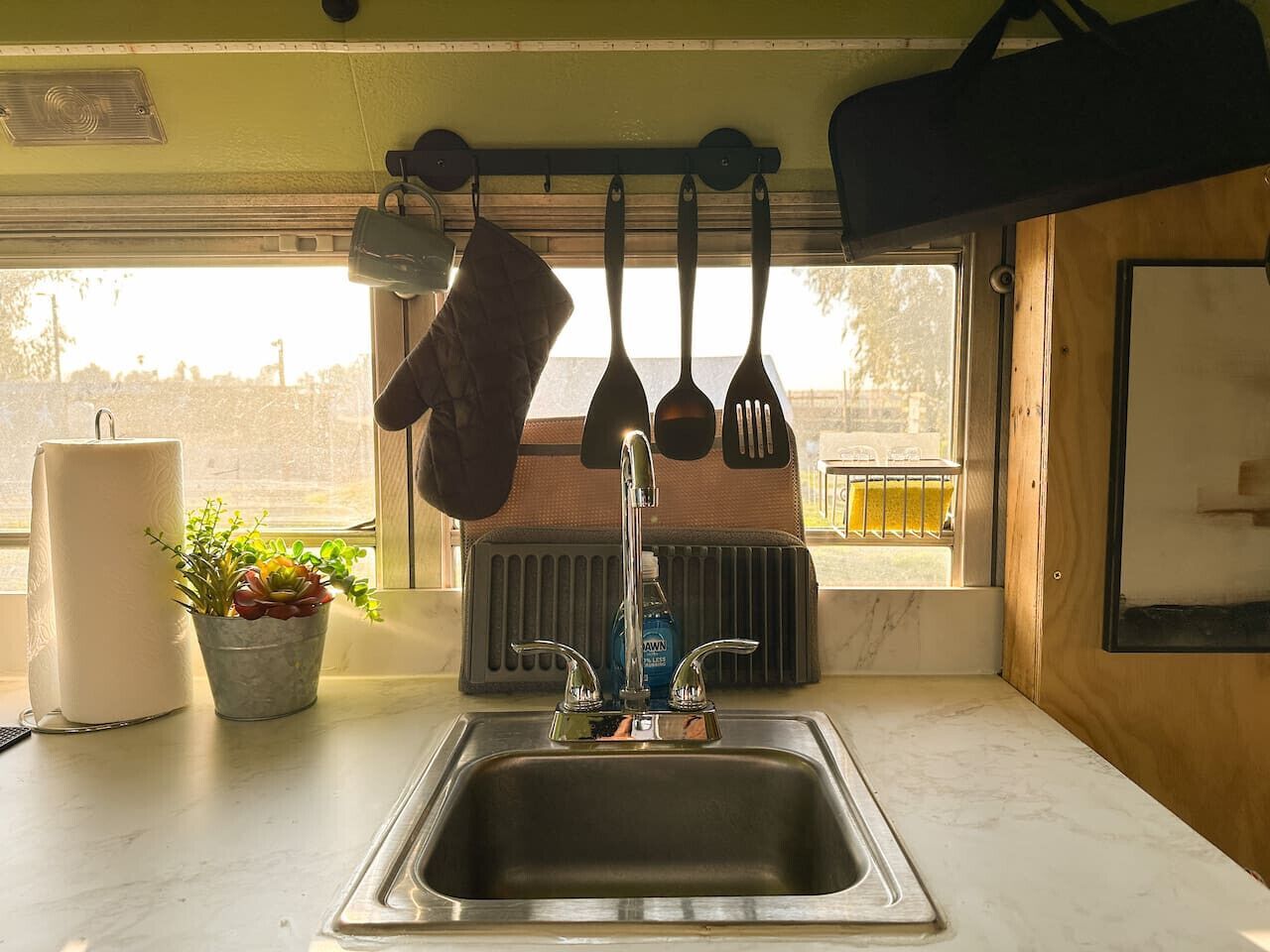 Una cocina con un lavabo, utensilios colgantes, una planta en maceta y una ventana con vistas.