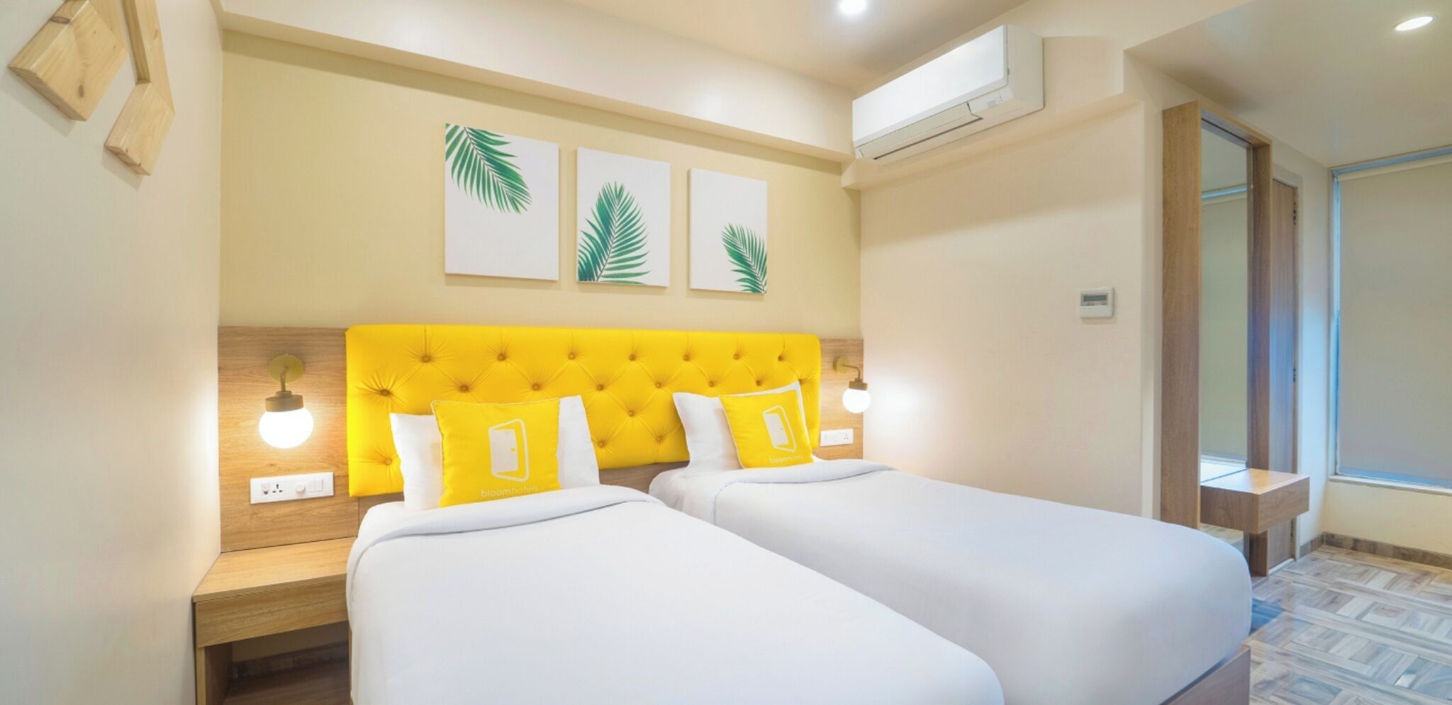 Een hotelkamer met twee bedden, een geel hoofdeinde en drie kunstwerken van palmbladeren.