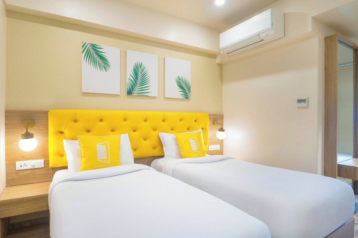 A hotel room with two beds, a yellow headboard, and three palm leaf wall art pieces.