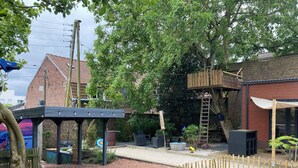 Un jardin avec une clôture en bois, une pergola et un bâtiment en briques en arrière-plan.
