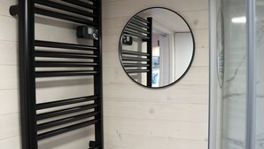 Une salle de bain avec un porte-serviettes noir, un miroir rond et une cabine de douche en verre.