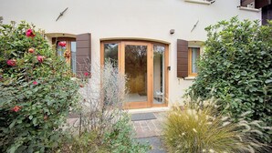Ein Haus mit einer bogenförmigen Holztür, einer kleinen Veranda und einem Garten mit verschiedenen Pflanzen und Blumen.