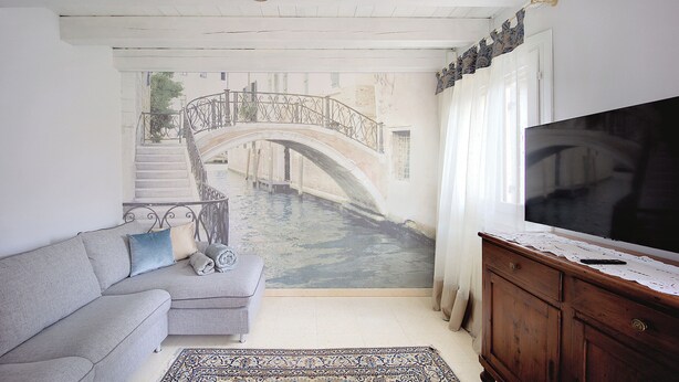 Ein Wohnzimmer mit Wandgemälde einer Brücke, einem Sofa, einem Fernseher und einem Holzschrank.