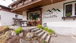 Un chalet llamado 'Chalet Charlotte' con fachada de madera, una zona de comedor con sillas y una mesa, y una escalera de piedra que conduce a la entrada.