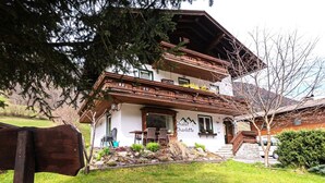 Un edificio de estilo chalé tradicional con balcón de madera, una escalera de piedra y un jardín bien cuidado.