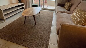 En stue med sofa, sofabord, fjernsyn og en balkon med bord og stole.