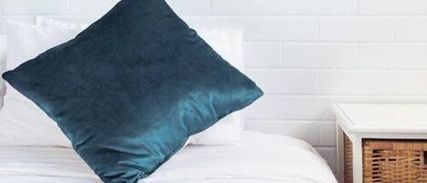 A bed with a teal pillow, white bedding, and a blue blanket.