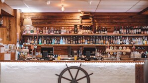 Een bar met houten wanden, flessenkasten vol drank en een decoratie van een scheepsschroef.