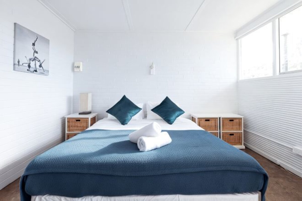 A bedroom with a large bed, two nightstands, a window, and a wall-mounted light.