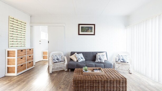 Een woonkamer met een grijze bank, een rieten salontafel, rieten bijzettafels, rieten manden en een ingelijst beeld aan de muur.