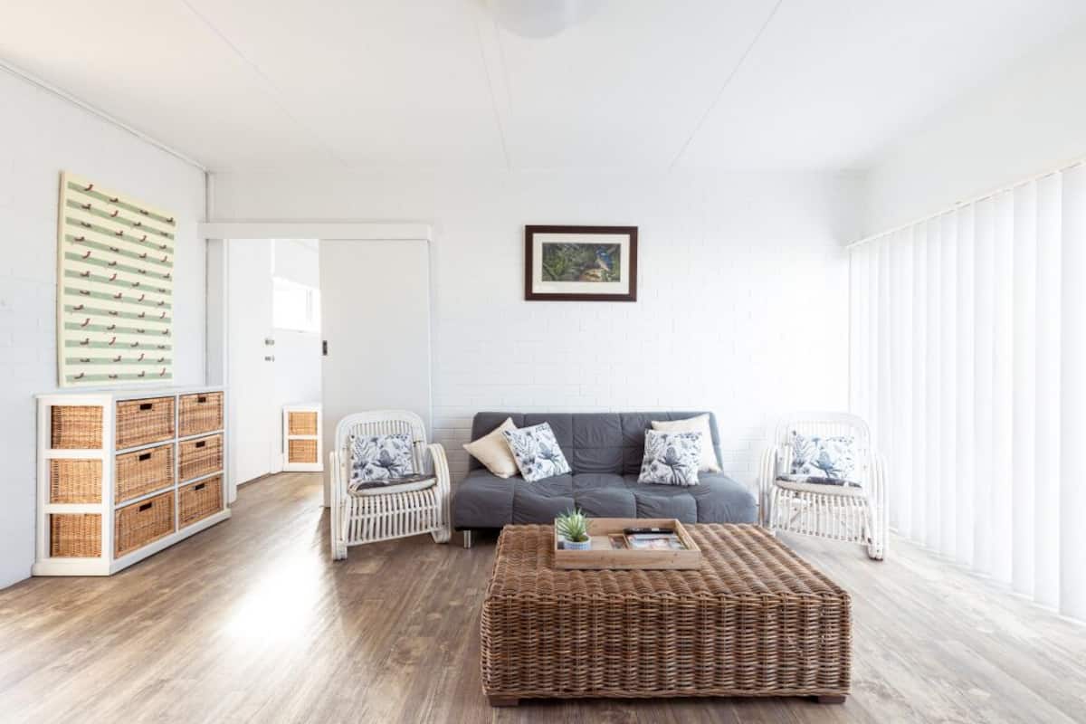 A living room with a grey sofa, wicker coffee table, wicker side tables, wicker baskets, and a framed picture on the wall.