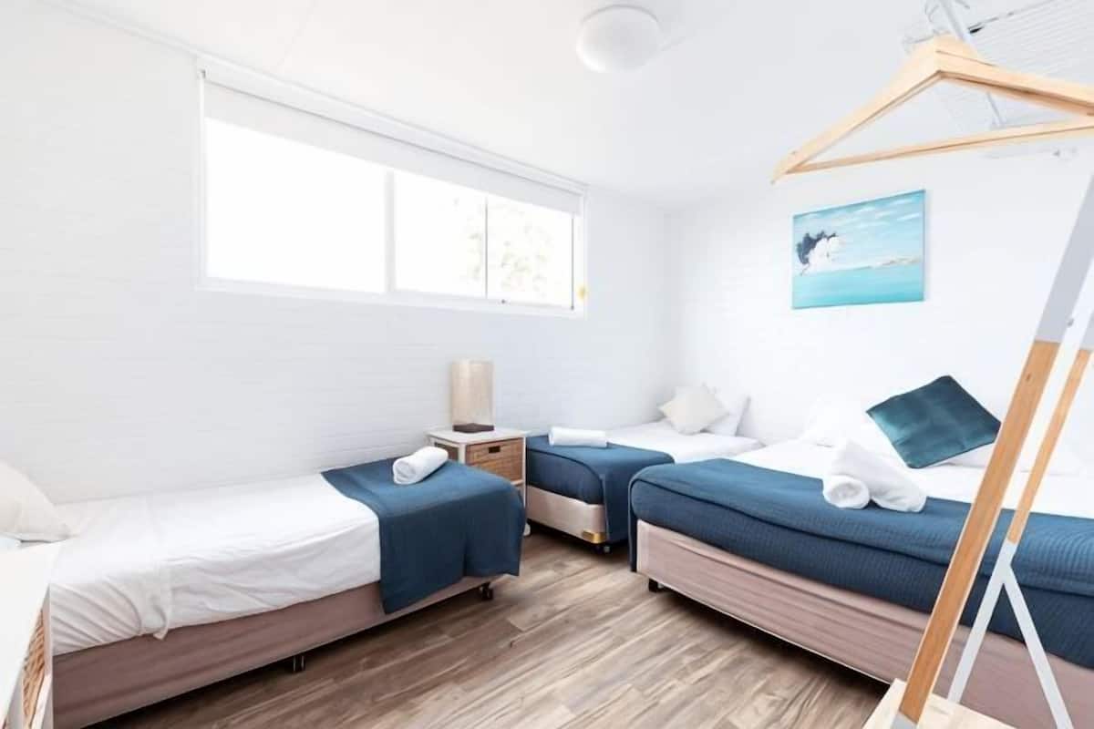 A room with two beds, a window, a painting, and a wooden floor.