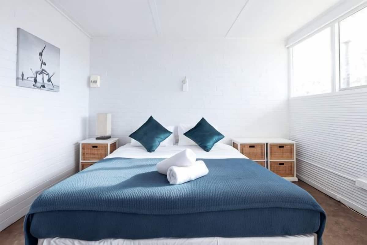 A bedroom with a large bed, two nightstands, a window, and a wall-mounted light.