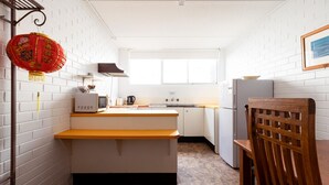 Een kleine keuken met witte bakstenen muren, een houten bankje, een gootsteen, een fornuis en een koelkast.