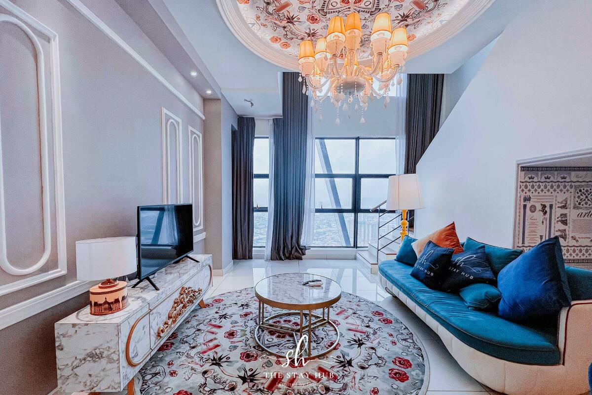 A modern living room with a round coffee table, a sofa with blue cushions, a television, and a chandelier.
