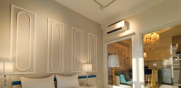 Una habitación de hotel con cama, escritorio, silla, lámpara, unidad de aire acondicionado y candelabro.