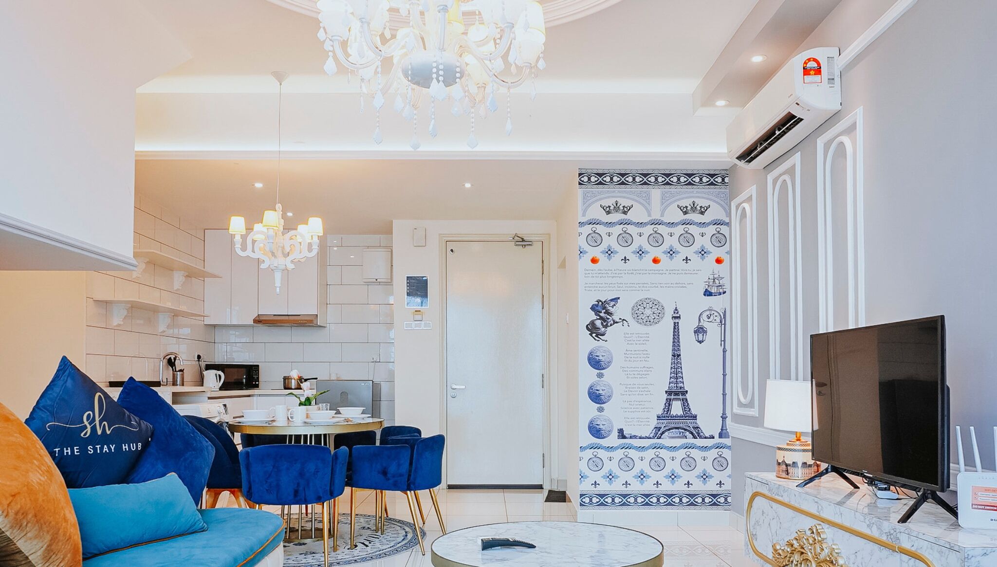 A modern living room with a blue sofa, chandelier, and a TV.