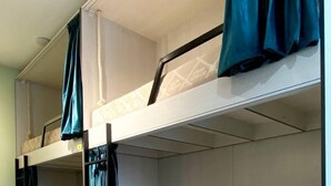A bunk bed room with two beds, each with a curtain. There are drawers under the beds and a ceiling light fixture.