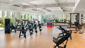 Academia moderna com máquinas de cardio, equipamentos de musculação e uma grande janela com vista para o verde.