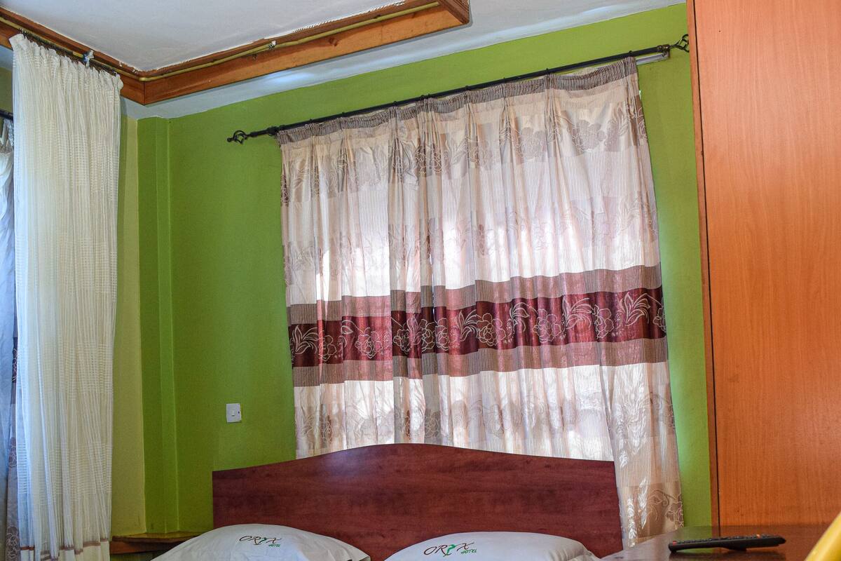 Un dormitorio con cama, una silla, un ventanal con cortinas y un armario de madera.