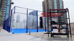 Una palestra all'aperto con attrezzature per esercizi, un sacco da boxe e un'area con tappetini blu, circondata da edifici alti.
