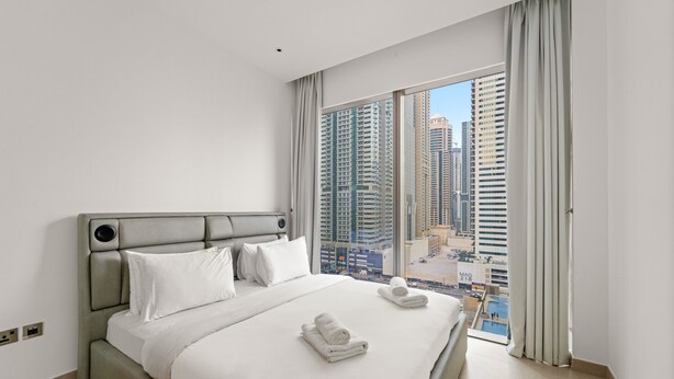 Una camera d'albergo moderna con un letto grande, lenzuola bianche e vista su edifici alti.