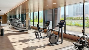 Een moderne sportschool met meerdere loopbanden en trainingsfietsen, grote ramen met uitzicht op een stadslandschap en groen.