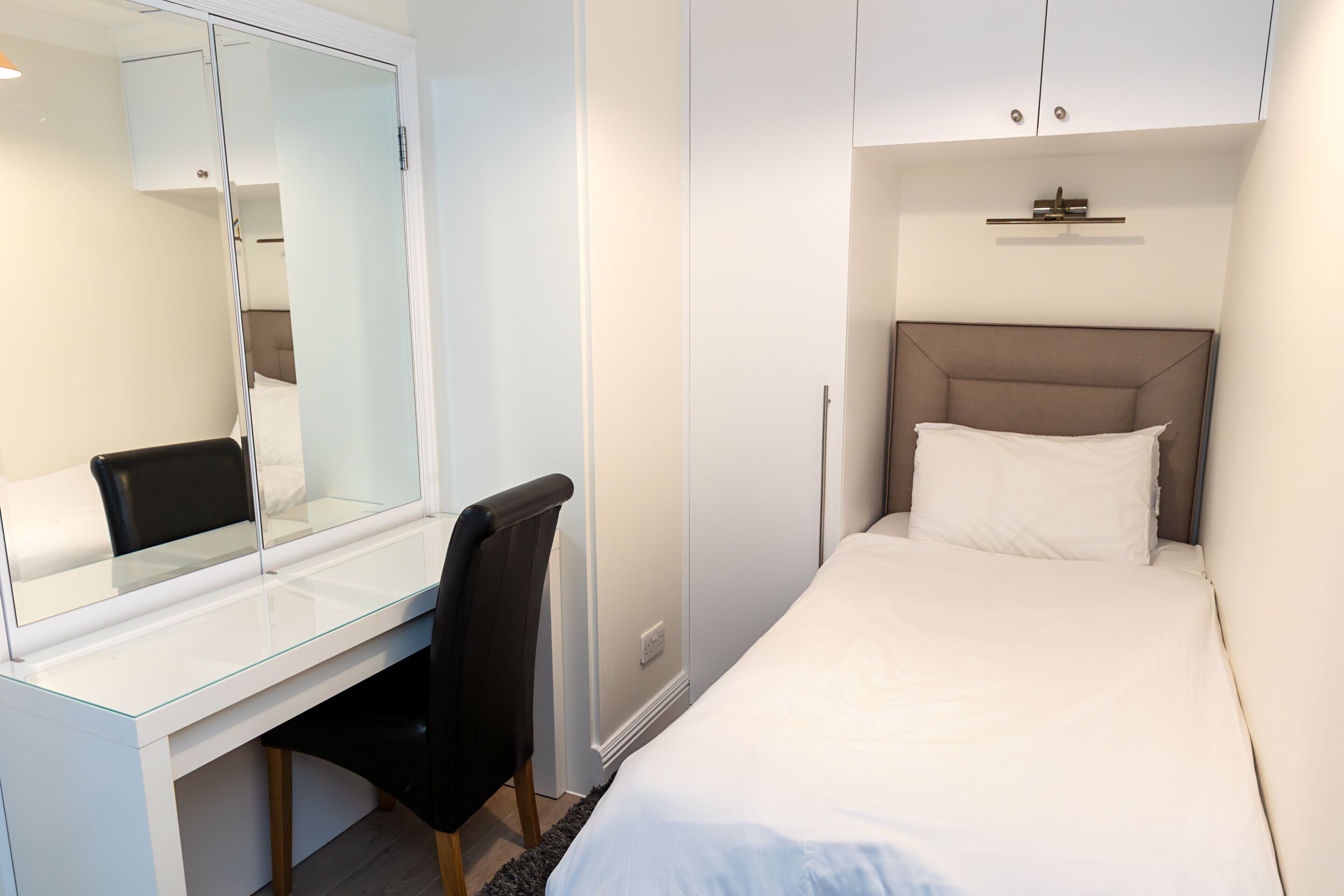 Ein Schlafzimmer mit einem Bett, einem Schreibtisch, einem Stuhl und einem Spiegel.