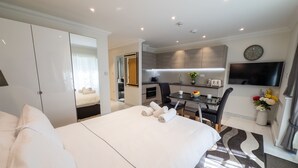 Une chambre d’hôtel moderne dotée d’un grand lit, d’un coin repas séparé, d’une kitchenette, d’un téléviseur à écran plat et d’une horloge murale.