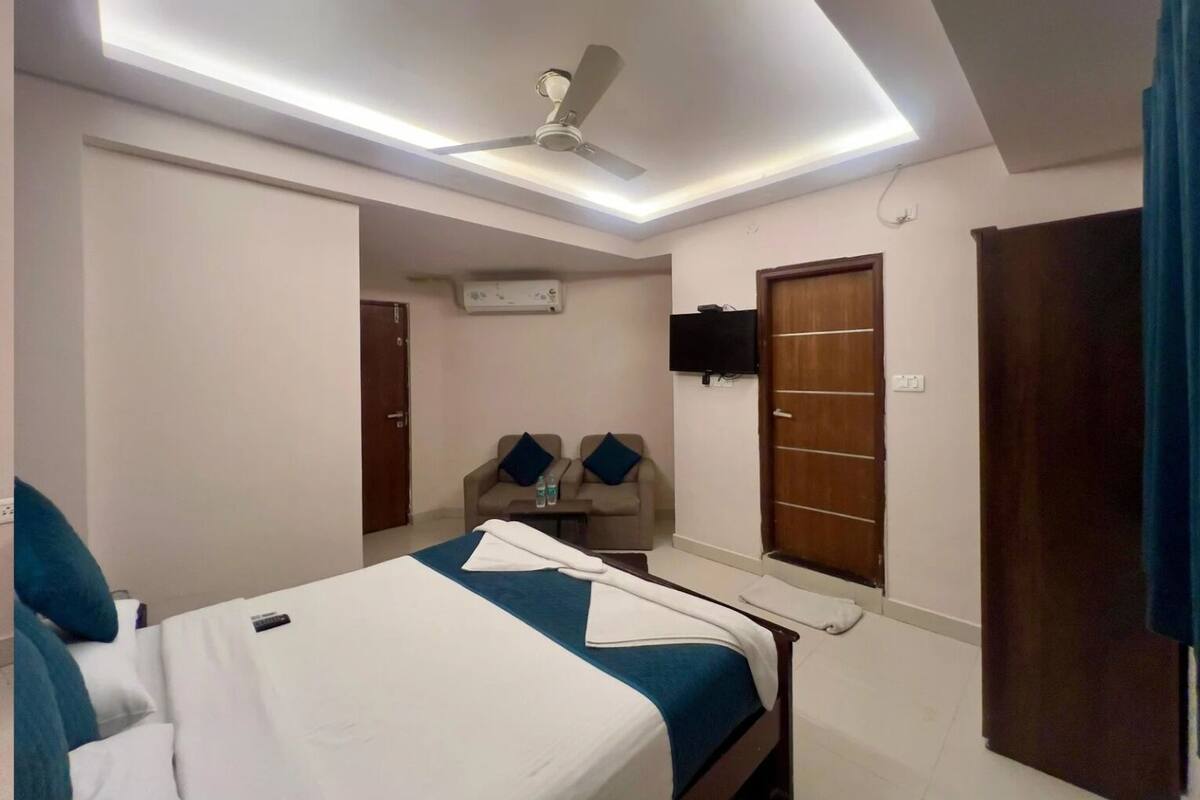 Une chambre d’hôtel avec un lit, un ventilateur de plafond, une télévision et une porte.