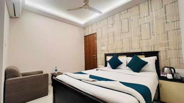 A hotel room with a bed, a chair, a nightstand, a water bottle, and a ceiling fan. - Blue Bliss Suites By PPH Living  (Bengaluru)