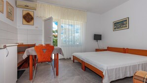 Ein Zimmer mit einem Bett, einem Schreibtisch mit Stuhl, einem Fernseher und einem Fenster mit Vorhängen.