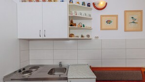Eine Küche mit weißen Schränken, einer doppelten Spüle und einem Herd. Über der Spüle befinden sich Regale mit Dekoration und zwei gerahmte Bilder an der Wand.