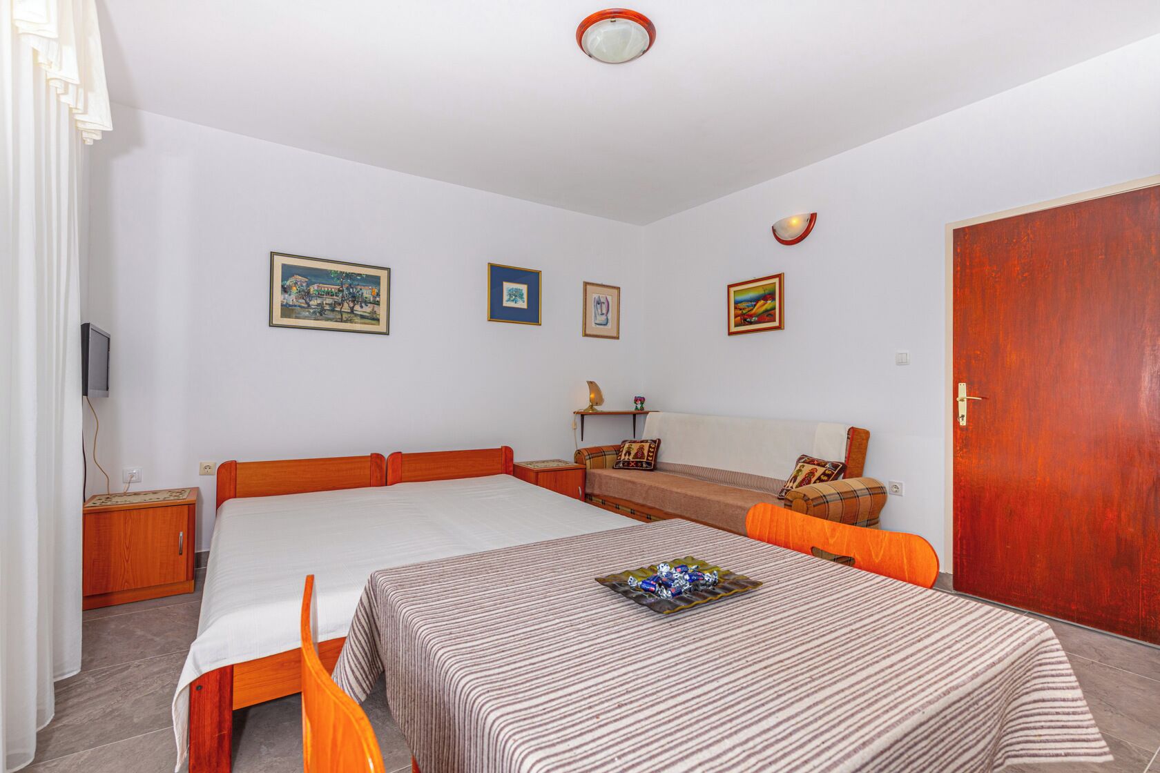 A bedroom with a large bed, a sofa, a television, and framed pictures on the wall.