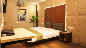 Un dormitorio con cama, mesita de noche, lámpara y televisor montado en la pared.