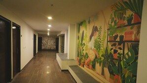 Un pasillo con suelo de madera, una escalera y un mural con ilustraciones de plantas en la pared.