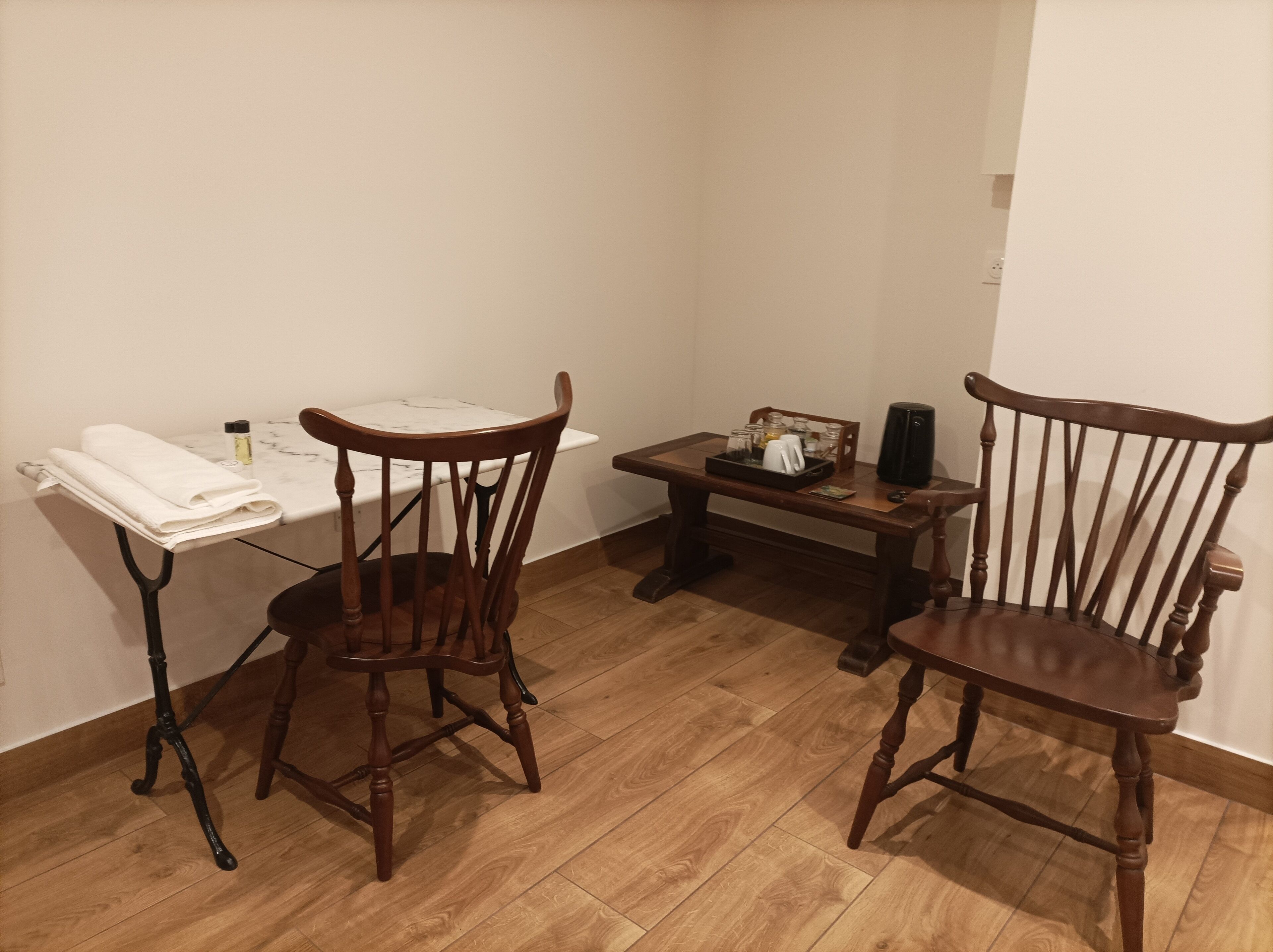 Una habitación con dos sillas de madera, una mesita con una bandeja y una mesa blanca con encimera de mármol.