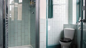 A bathroom with a glass-enclosed shower, a white toilet, and tiled walls. - The Ship Rooms (London)
