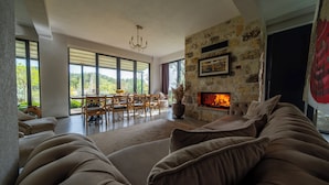 A modern living room with a stone fireplace, large windows, and a cozy sofa. - Assosa Country House (Ayvacik)