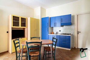 A compact kitchen with yellow and blue cabinets, a wooden dining table, and four chairs. - Hotiday Apartment Collection-Pugnochiuso (Vieste)