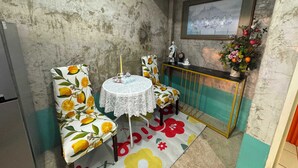 A small, rustic room with a round table and two chairs, a small console table with a vase of flowers, and a framed picture on the wall. - OYO 75539 Phanthida Resort and Cafe (Pranburi)
