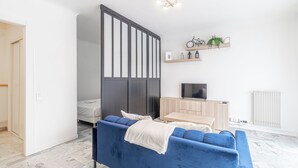 Ein modernes Wohnzimmer mit einem blauen Sofa, einem Holz-TV-Möbel und einem Wandregal mit Pflanzen und einem Fahrrad.