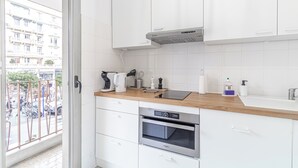 Eine moderne Küche mit weißen Schränken, einer Holzarbeitsplatte, einem eingebauten Backofen und einem Fenster mit Blick auf eine Straße.